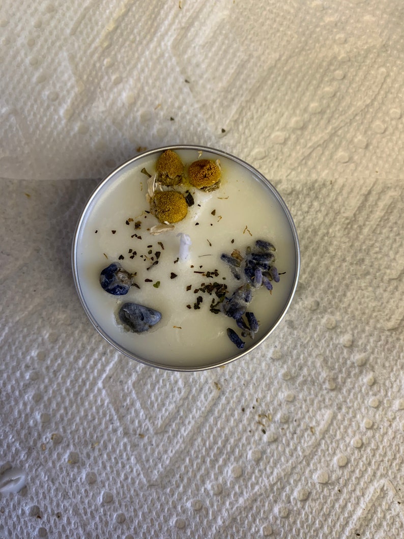 May include: A white candle with dried lavender, chamomile, and blue stones embedded in the wax.