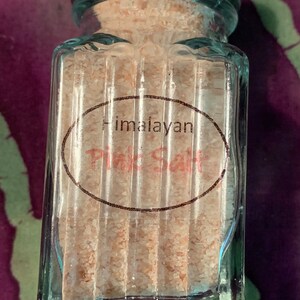 May include: A glass jar with a silver lid filled with pink Himalayan salt. The jar has a label that reads "Himalayan Pink Salt".