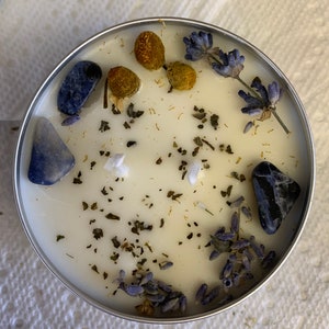 May include: A white candle with dried lavender, dried chamomile, and blue stones embedded in the wax.