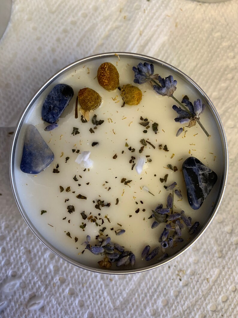 May include: A white candle with dried lavender, dried chamomile, and blue stones embedded in the wax.