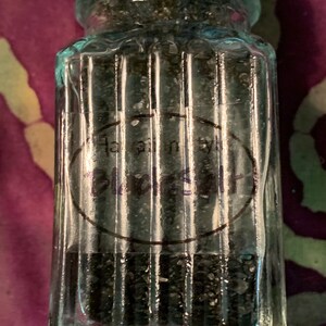 May include: A glass jar with a silver lid filled with black salt. The jar has a label that reads "Hawaiian Black Salt".