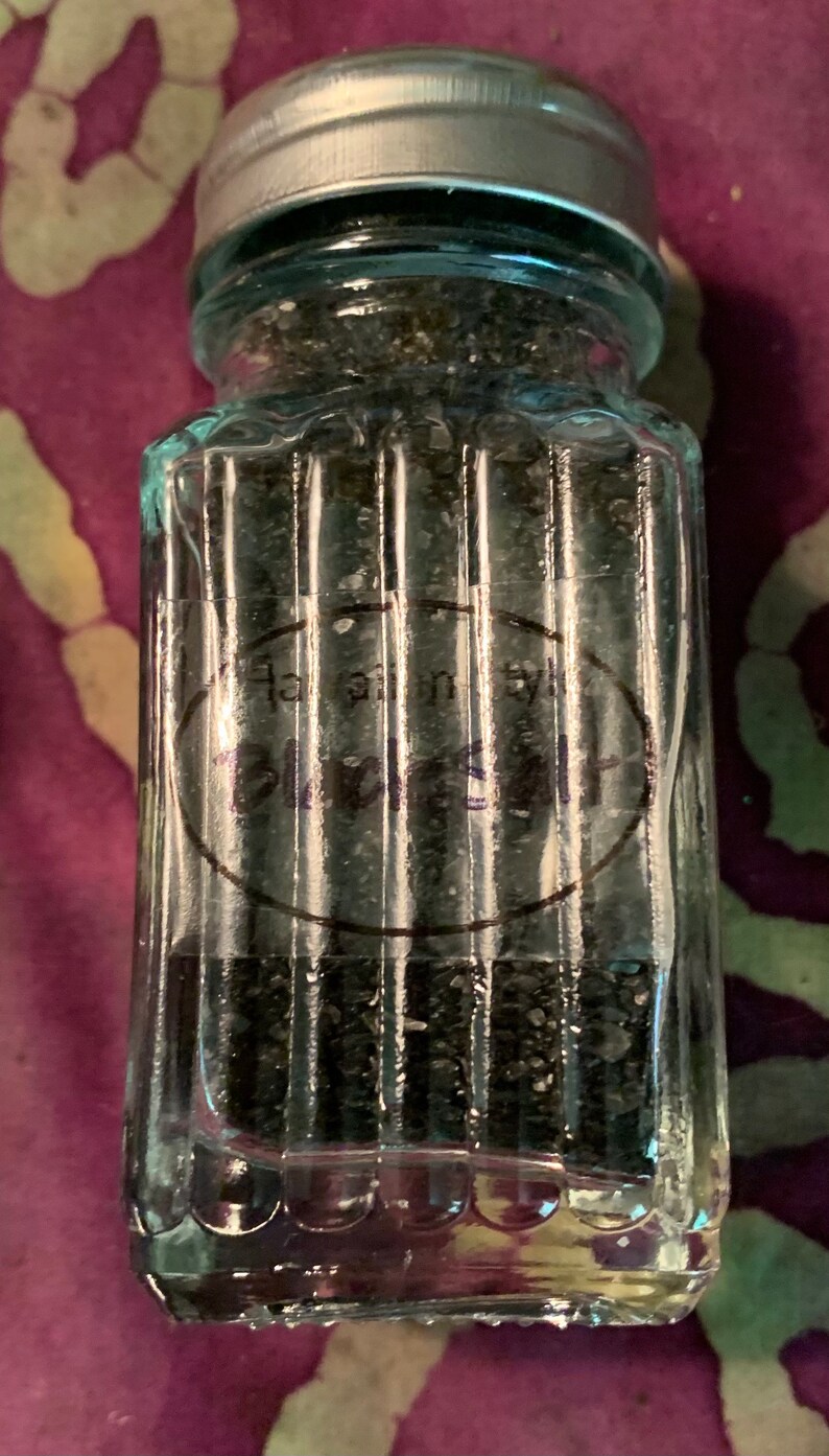 May include: A glass jar with a silver lid filled with black salt. The jar has a label that reads "Hawaiian Black Salt".