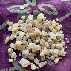 May include: A pile of light brown and white resin pieces on a purple fabric background. The resin pieces are irregular in shape and size.