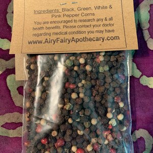 May include: A close-up of a bag of four-color whole peppercorns. The peppercorns are black, green, white, and pink. The bag is labeled "4 Color Whole Pepper" and includes the ingredients: "Black, Green, White & Pink Pepper Corns". The label also includes the website address: "www.AiryFairyApothecary.com".