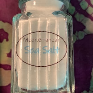 May include: A clear glass jar with a silver lid filled with white sea salt. The jar has a label that reads "Mediterranean Sea Salt".