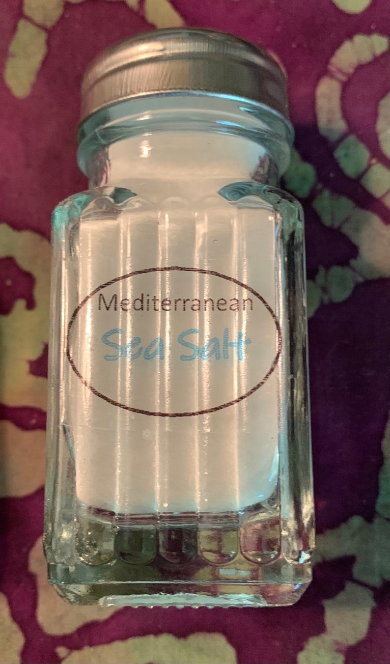 May include: A clear glass jar with a silver lid filled with white sea salt. The jar has a label that reads "Mediterranean Sea Salt".