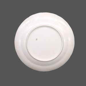 Puede incluir: Plato de cer&aacute;mica blanco con borde dorado y una peque&ntilde;a marca de estrella de tres puntas de color marr&oacute;n en la parte inferior.