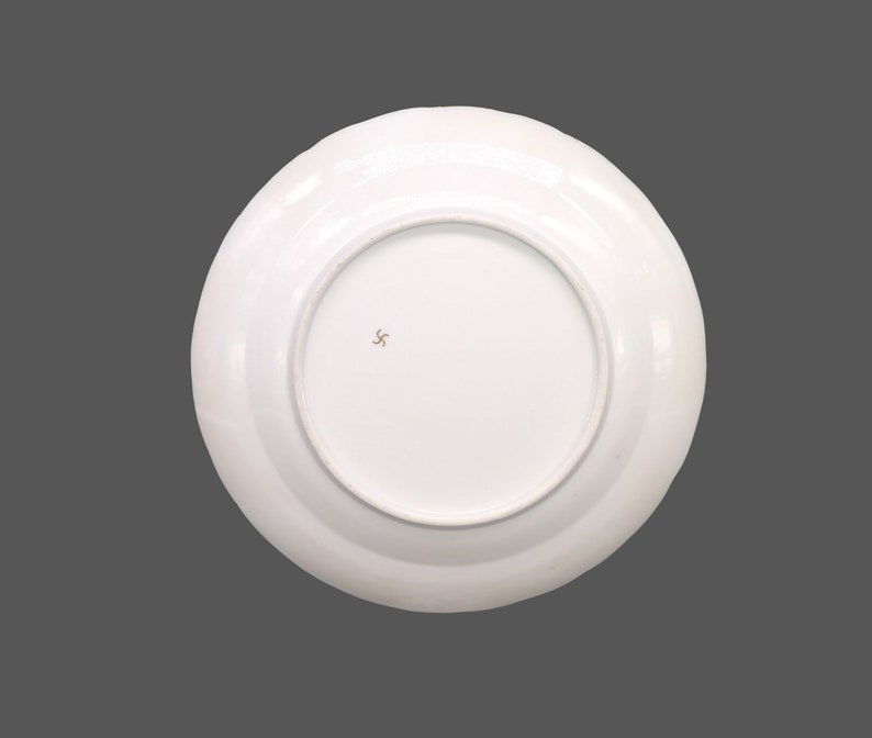 Puede incluir: Plato de cer&aacute;mica blanco con borde dorado y una peque&ntilde;a marca de estrella de tres puntas de color marr&oacute;n en la parte inferior.