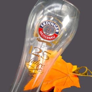 May include: A clear glass beer stein with a gold inscription that reads "25 Jahre" and a blue and white logo that says "Erdinger Weissbrau".