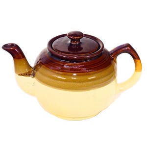 May include: A brown and cream ceramic teapot with a lid. The teapot has a rounded body and a spout on the side.
