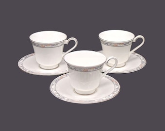 May include: Set of three white porcelain teacups and saucers with a floral design in shades of blue, pink, and gold.