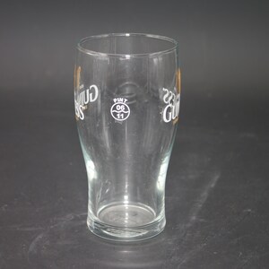 May include: A clear glass pint glass with the Guinness logo printed on the side. The logo is in gold and black and includes the text "Guinness" and "Dublin, Ireland". The glass also has a white circle with the text "Pint 0.6 11" printed on the side.