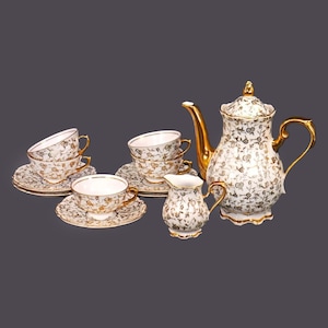 May include: A white tea set with gold accents and floral patterns. The set includes a teapot, creamer, and four cups and saucers.