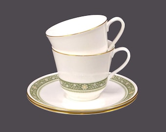 May include: Two white teacups with green and white floral designs and gold trim stacked on top of each other on a matching saucer.