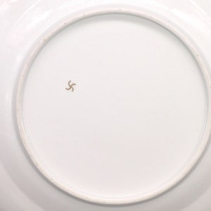 Puede incluir: La parte inferior de un plato de cer&aacute;mica blanco con una marca de estrella dorada de cinco puntas en el centro.
