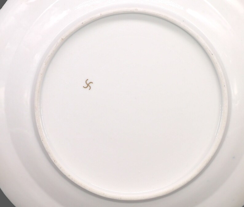 Puede incluir: La parte inferior de un plato de cer&aacute;mica blanco con una marca de estrella dorada de cinco puntas en el centro.