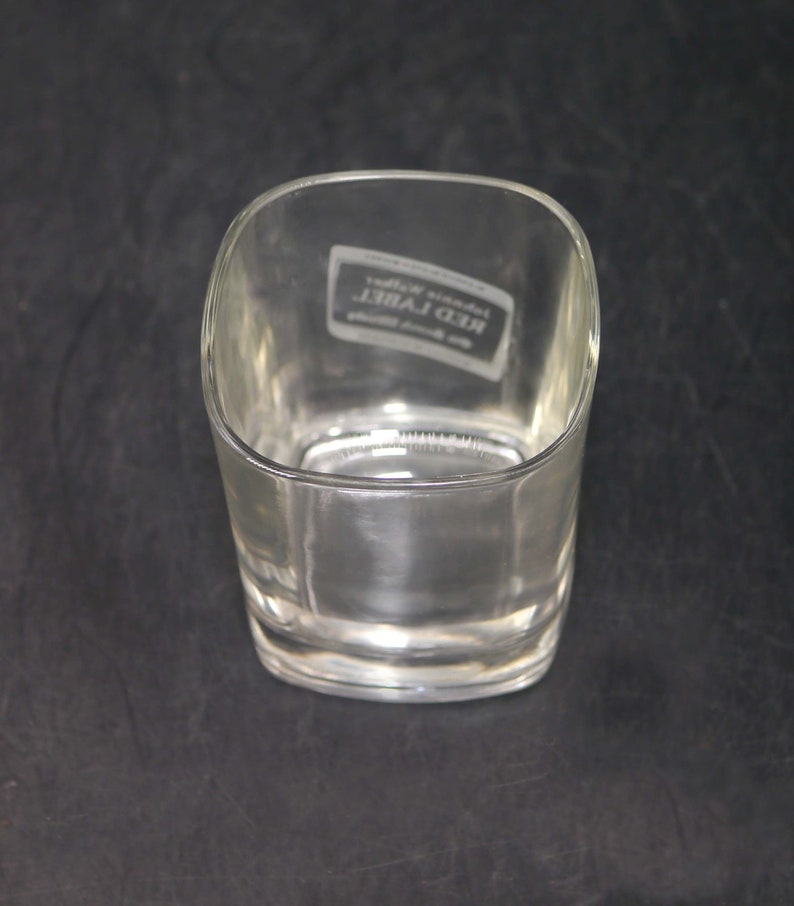 Peut inclure: Un verre &agrave; whisky en verre transparent avec une base carr&eacute;e et des bords arrondis. Le verre porte l'inscription "Johnnie Walker Red Label" grav&eacute;e au fond.