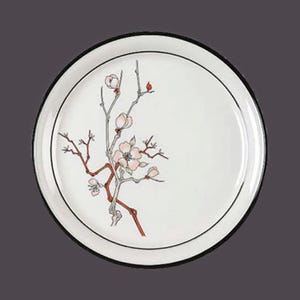 May include: A white ceramic plate with a black rim features a delicate floral design of a pink blossom branch with red stems. The plate is ideal for serving a variety of dishes.