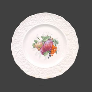 May include: White ceramic plate with a raised, embossed border. The center of the plate features a painted design of plums, apples, and berries.