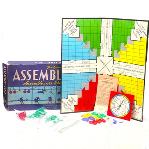 May include: A vintage board game called "The Game Assembly Line" with a blue box and a colorful game board. The game board has a grid with different colored squares and the text "Chevrolet Assembly Line" and "Plymouth Assembly Line". The game includes a spinner, dice, and small plastic pieces.