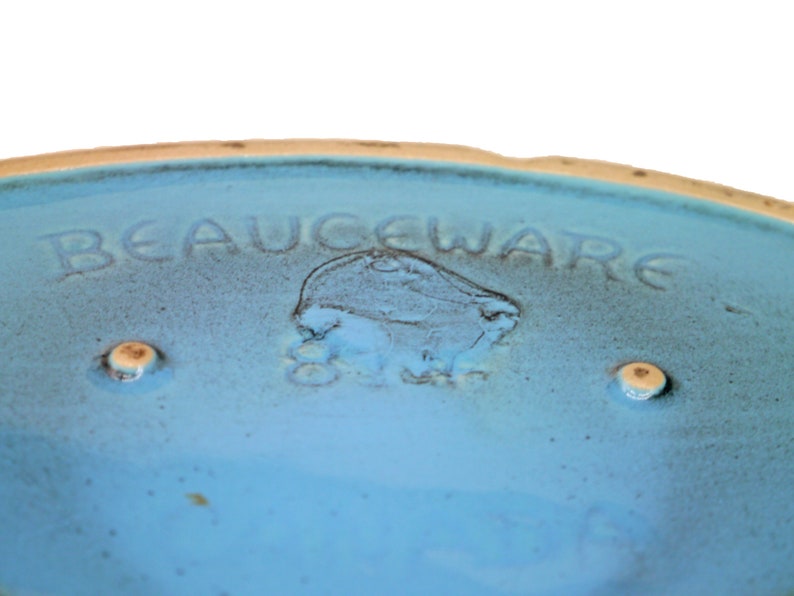 以下が含まれることがあります： 薄い青色のセラミックボウルで、底に「BEAUCEWARE」という文字が刻まれています。ボウルは薄い茶色の縁取りがあり、底に2つの小さな丸い薄い茶色の点があります。