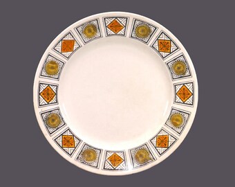 May include: A white ceramic plate with a decorative border of orange, yellow, and black geometric shapes.