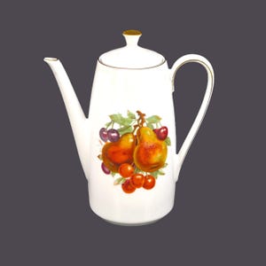 May include: White ceramic coffee pot with a gold trim and a fruit design. The design features two pears and cherries in shades of red, orange, and purple.