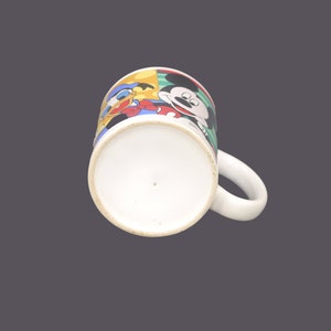 May include: A white ceramic mug with a colorful cartoon design featuring Mickey Mouse, Donald Duck, and Goofy. The mug has a handle and a white interior.