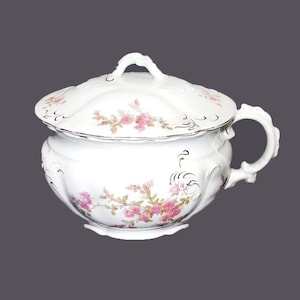 May include: A white porcelain chamber pot with a lid, featuring a floral design with pink and gold accents.