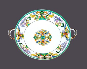 May include: A white ceramic serving bowl with green, yellow and blue floral designs. The bowl has two gold handles and a gold rim.