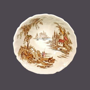 May include: A white ceramic bowl with a brown and green landscape scene. The scene features a river, a watermill, trees, and a couple of figures. The bowl has a scalloped edge.