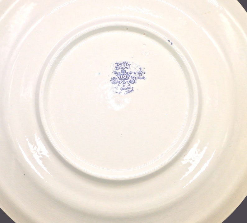 May include: A white ceramic plate with a blue and white Delft Blue logo that reads "Delft Blau" and "Hand painted Holland".