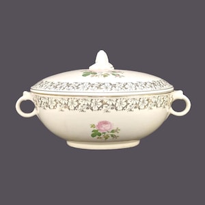 May include: A white ceramic serving bowl with a lid, featuring a floral design with pink roses and gold accents. The bowl has two handles on the sides.