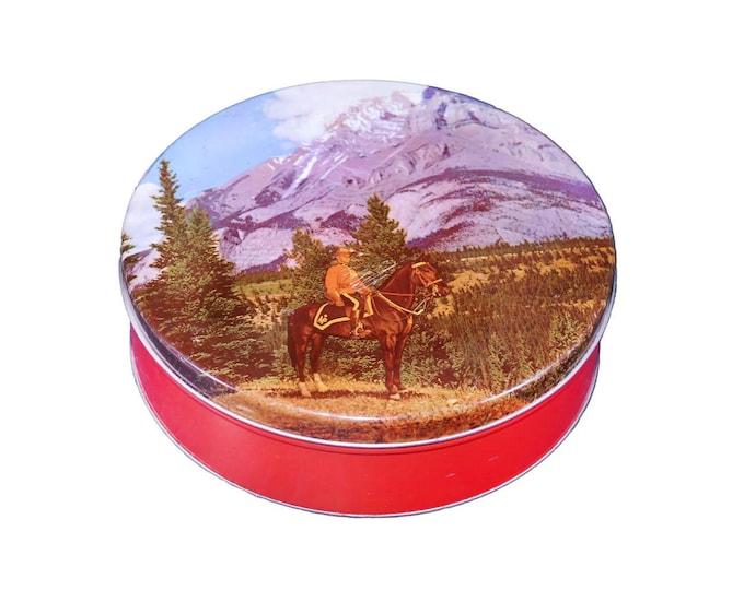 Round cookie biscuit tin. Canadian Mountie on horseback, trees mountains in background.