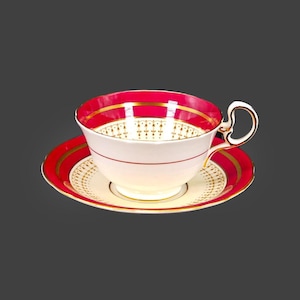 May include: A white teacup and saucer with a gold and red trim. The saucer features a delicate floral pattern.