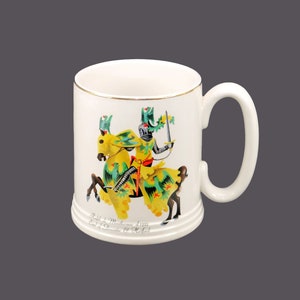 May include: White ceramic mug with a gold rim. The mug features a colorful illustration of a knight on horseback. The text on the mug reads "Sir John de Mowbray 1323 Earl of Nottingham & Marshal".