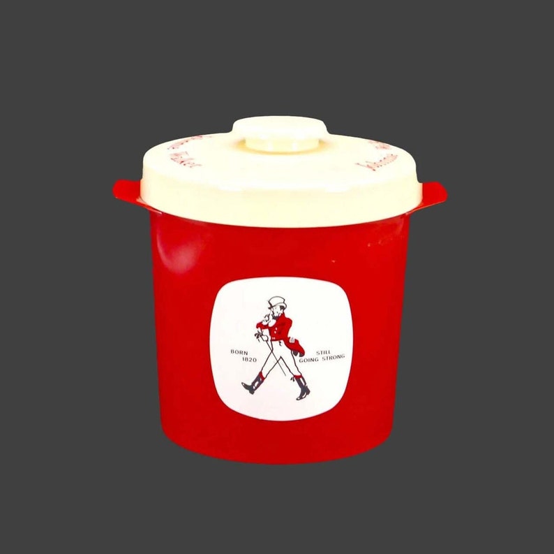 May include: Red plastic container with a white lid and a Johnnie Walker logo. The logo features a man in a top hat walking with a stick and the text "Born 1820 Still Going Strong".