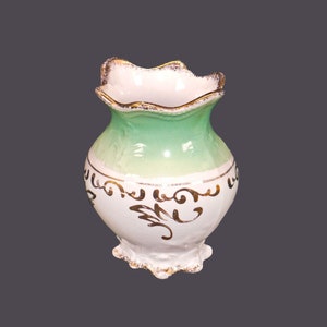 May include: A small, white ceramic vase with a green glaze and gold accents. The vase has a scalloped rim and a decorative floral design.