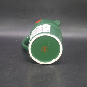 May include: Green ceramic pitcher with a white label that says "Johnnie Walker Red Label Scotch Whisky" and a red circle with a letter "E" in the center of the bottom.