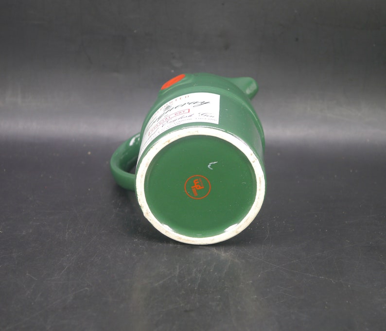 May include: Green ceramic pitcher with a white label that says "Johnnie Walker Red Label Scotch Whisky" and a red circle with a letter "E" in the center of the bottom.