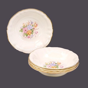 May include: A set of cream-coloured bowls featuring a floral design in the centre. The flowers are in shades of pink, yellow, and purple. The rims have a gold trim. The bowls have a scalloped edge.