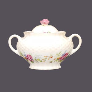 Puede incluir: Azucarero de cerámica blanca con un diseño floral y una rosa rosa en la tapa. El tazón tiene un patrón tejido y un delicado diseño floral.