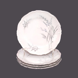 May include: Set of four white porcelain dinner plates featuring a delicate floral design in shades of grey. The plates have a scalloped edge and a subtle sheen.