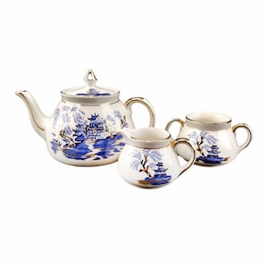 May include: A white porcelain tea set with a blue and gold Asian-inspired design. The set includes a teapot, a creamer, and a sugar bowl. The teapot has a lid and a gold handle. The creamer and sugar bowl have gold trim.