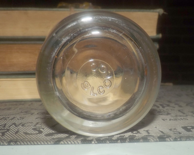 May include: Clear glass bottle with a textured surface and a circular label that reads "ELCO".