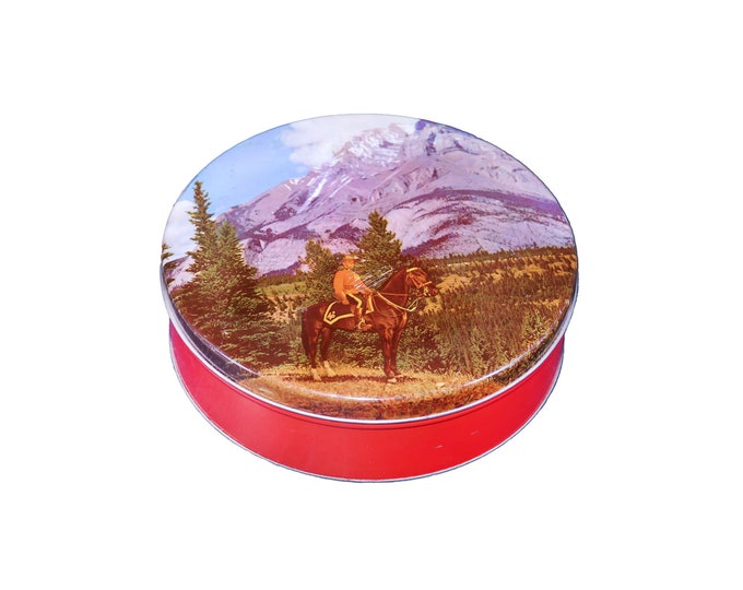 Round cookie biscuit tin. Canadian Mountie on horseback, trees mountains in background.