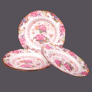 May include: Three white porcelain plates with a pink and green floral pattern. The plates are stacked on top of each other.