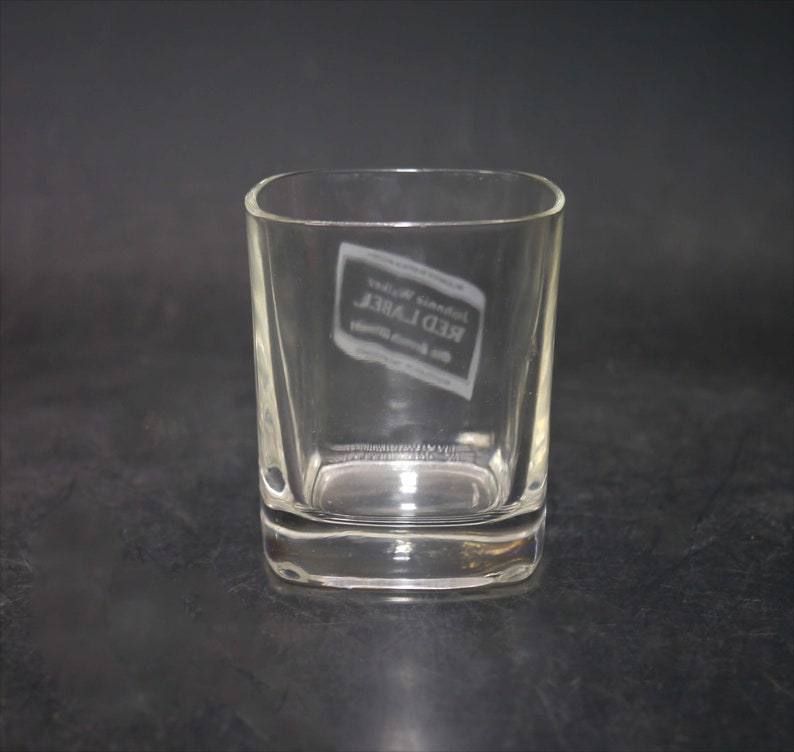 Peut inclure: Un verre &agrave; whisky en verre transparent avec une base carr&eacute;e et des bords arrondis. Le verre porte l'inscription "Johnnie Walker Red Label" grav&eacute;e sur le c&ocirc;t&eacute;.