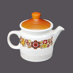May include: A white ceramic teapot with a brown lid and a floral design in shades of red, yellow, and brown.