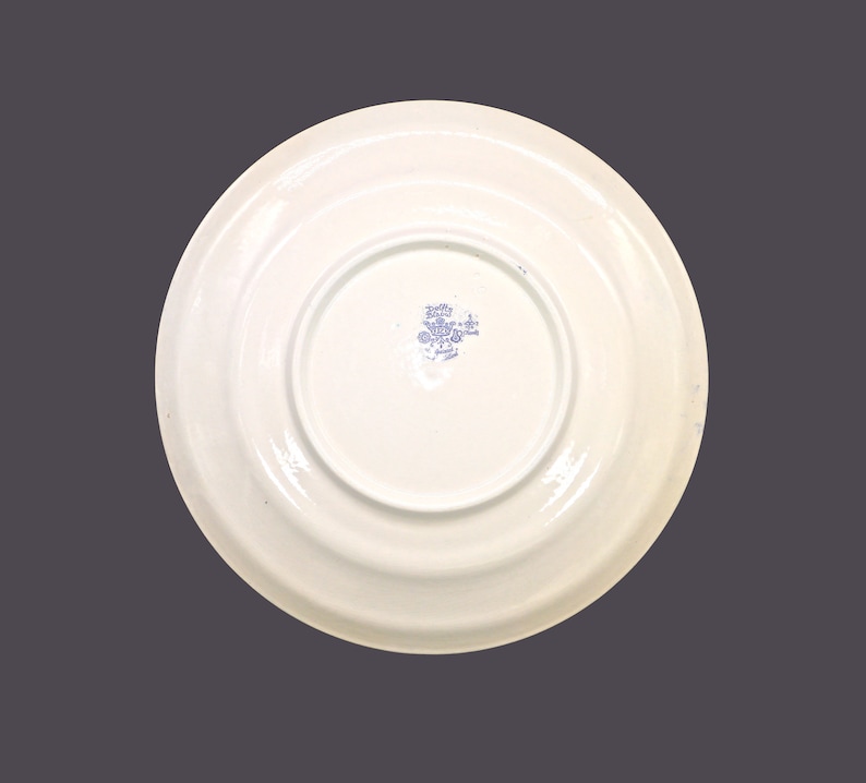 May include: The back of a white ceramic plate with a blue floral design and the text "Holly Hobbie - Made in Japan" in a blue circle.